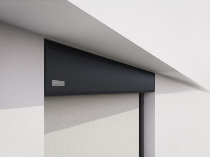 Detail view of a gray markilux vertical blind mounted in a niche of a white house wall.