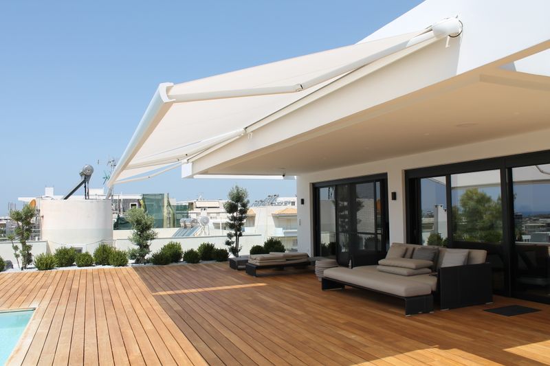 White cassette awning MX-3 over a wooden terrace by a pool in Greece.
