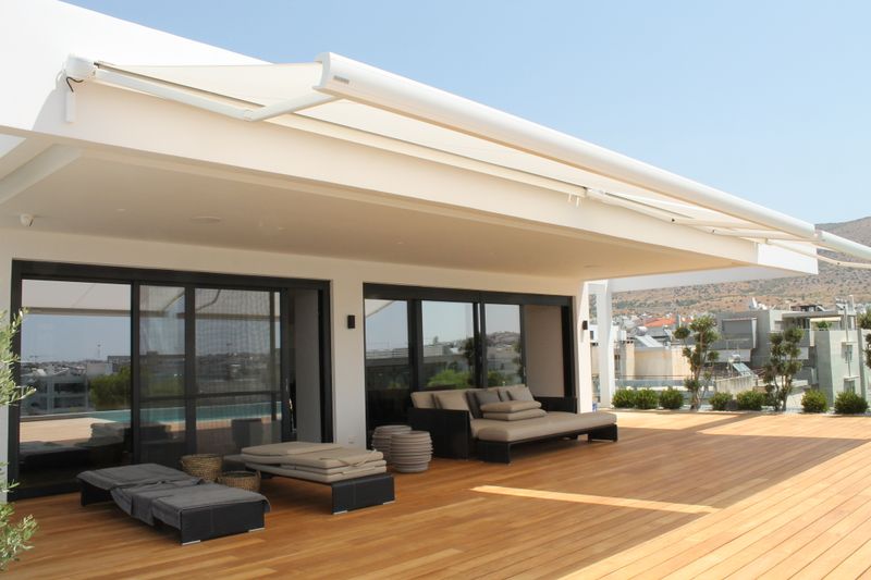 White cassette awning MX-3 over a wooden terrace by a pool in Greece.